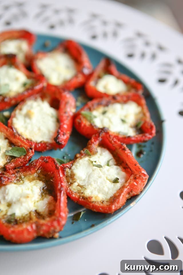 Beautifully arranged roasted red peppers with pesto and goat cheese on a plate, garnished with fresh herbs, suitable for a party or meal.