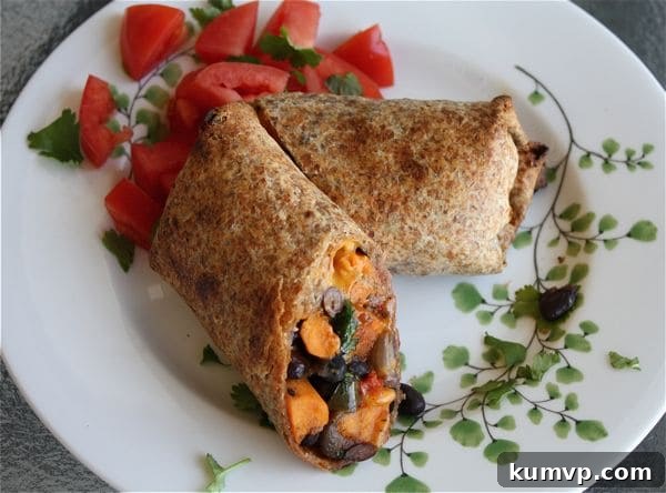 A savory sweet roasted veggie and black bean burrito, cut in half, revealing its vibrant filling of sweet potatoes, bell peppers, and black beans, served on a white plate. This delicious vegetarian meal is perfect for meat lovers too.