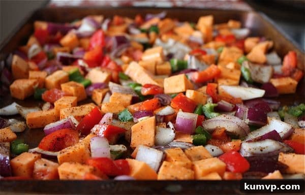 A sheet pan loaded with colorful, cubed sweet potatoes, red onions, and bell peppers, tossed in spices and olive oil, ready for roasting to create delicious roasted veggie and black bean burritos.