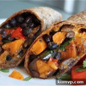 Two halves of a delicious sweet potato and black bean burrito, showcasing the rich, roasted vegetable filling and melted cheese, perfectly presented on a plate.