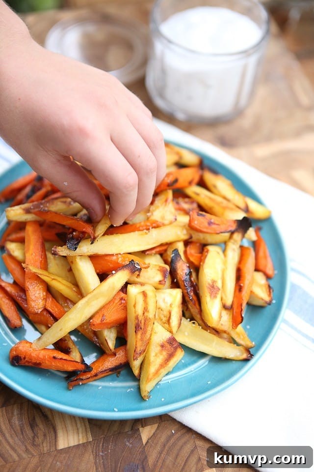 Honey Roasted Parsnips and Carrots - a delightful family favorite! Close-up of golden brown honey roasted parsnip and carrot sticks on a white baking sheet, demonstrating their kid-friendly appeal.