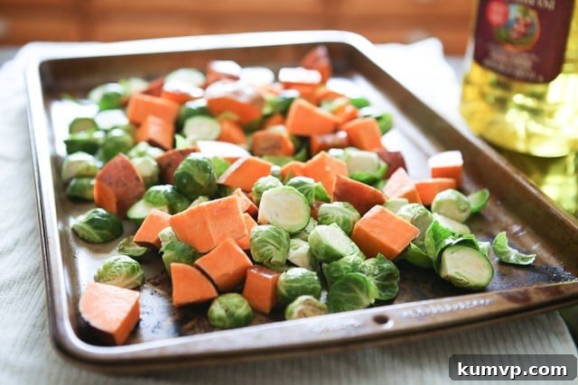 Prepped Sweet Potatoes and Brussels Sprouts for Roasting Sheet pan with uncooked cubed sweet potatoes and halved Brussels sprouts, tossed in oil, ready for roasting