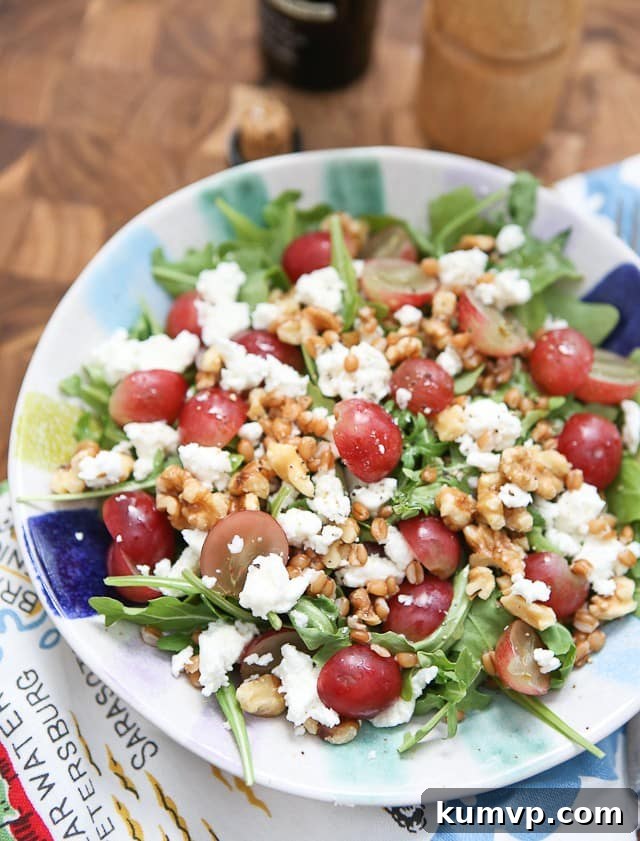 A vibrant and colorful Wheat Berry and Arugula Salad with fresh grapes, toasted walnuts, and crumbled goat cheese, elegantly arranged in a white serving bowl.