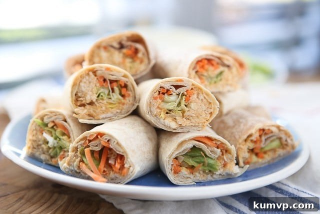 A beautifully presented plate of Buffalo Hummus Chicken Salad Roll Ups, halved and stacked with fresh vegetables visible, ready to be served.