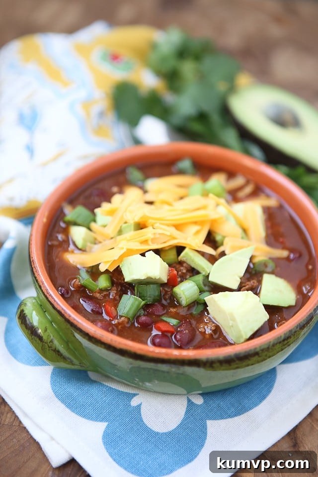 A hearty bowl of Chipotle Chicken Chili, richly colored, topped with shredded cheese, creamy avocado slices, and fresh green scallions, ready to be enjoyed.