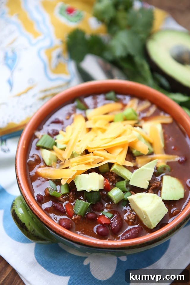 A serving of Chipotle Chicken Chili generously topped with tender shredded chicken, creamy diced avocado, and vibrant green scallions, showcasing a perfect combination of textures and fresh garnishes.