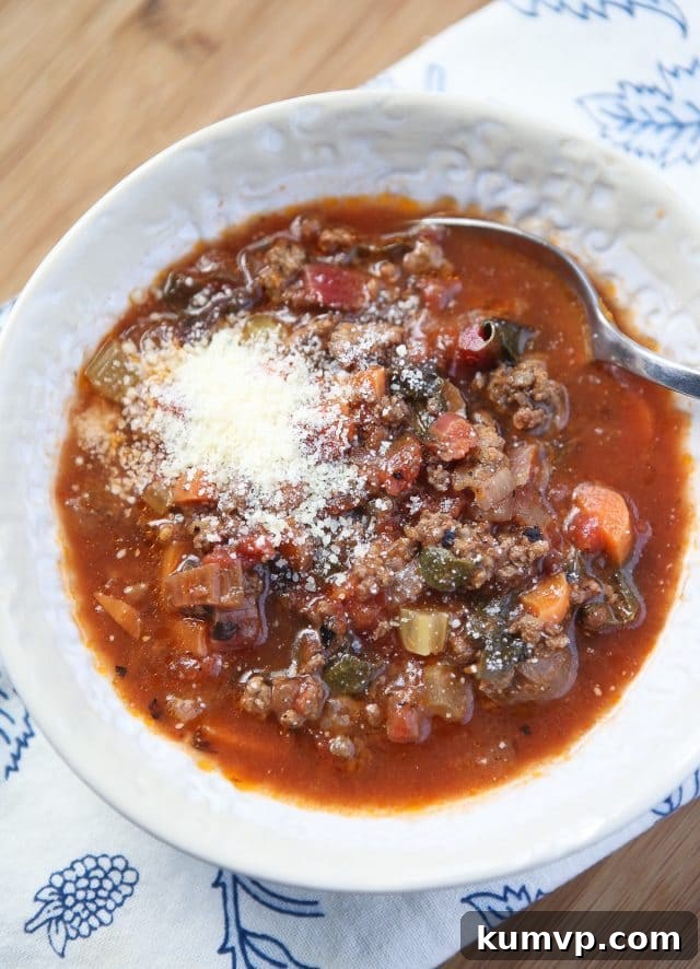 A close-up shot of a bowl of vegetable beef soup, garnished with freshly grated Parmesan cheese, highlighting its comforting warmth and robust ingredients.