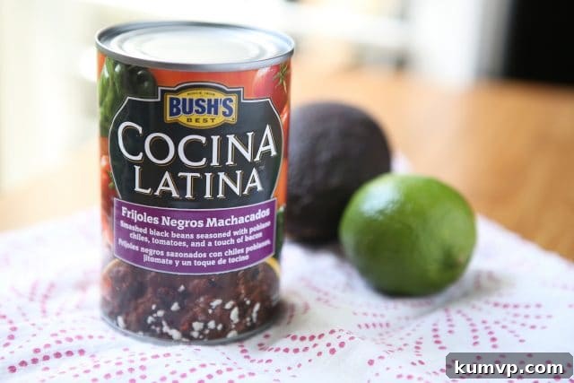 Can of Bush's Cocina Latina Frijoles Negros Machacados alongside fresh avocado and lime, highlighting key ingredients