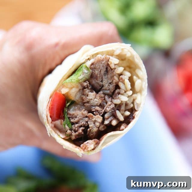 Hand holding a perfectly wrapped turkey and black bean burrito with a bite taken, revealing the delicious fillings