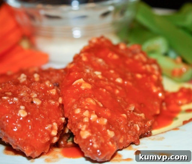 Hot and Garlic Baked Boneless Chicken Wings: A Healthier Zinger Alternative Two boneless chicken wings covered in hot sauce and minced garlic with celery & carrot sticks with a side of blue cheese in the background, ready to be enjoyed.