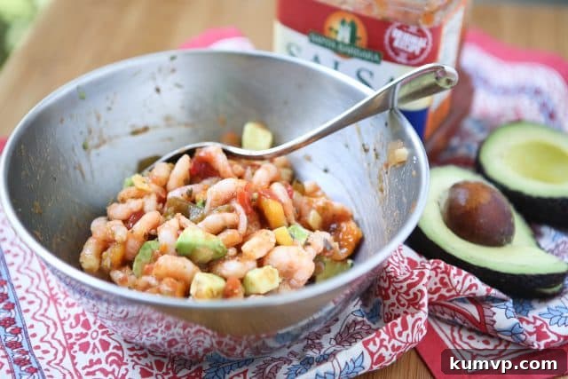 Mango Salsa Shrimp Tacos with Avocado A rustic bowl filled with seasoned shrimp, diced mango, and avocado, resting on a textured tapestry. A fresh avocado half and a small bowl of salsa are visible in the background.