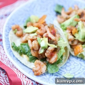 Two vibrant Mango Salsa Shrimp Tacos with creamy avocado on a white plate, garnished with fresh lime and cilantro.