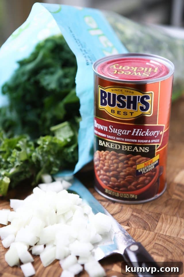 Key Ingredients for Baked Bean, Sausage and Kale Skillet can of Bush's brown sugar hickory baked beans, bunch of kale, and chopped white onions on a cutting board with a knife