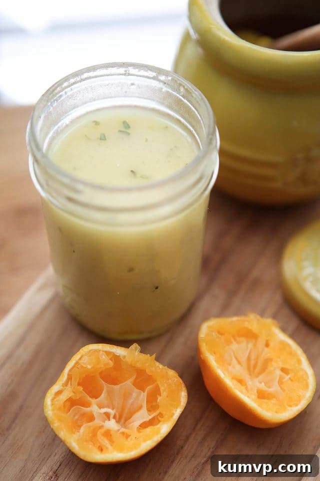 A mason jar filled with bright orange clementine vinaigrette sits on a rustic wooden cutting board, flanked by two freshly squeezed clementine halves, showcasing the fresh ingredients. The scene evokes freshness and healthy eating.