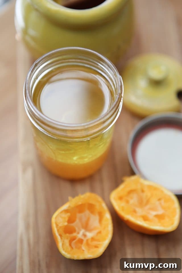 A second view of the clementine vinaigrette being prepared in a mason jar, with a freshly squeezed tangerine half nearby on a wooden cutting board. The focus is on the simple, natural ingredients.