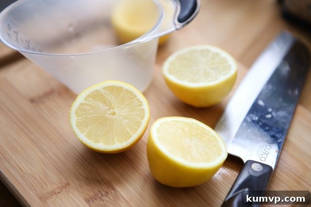 Two lemons sliced in half on wooden cutting board with a measuring cup and large knife