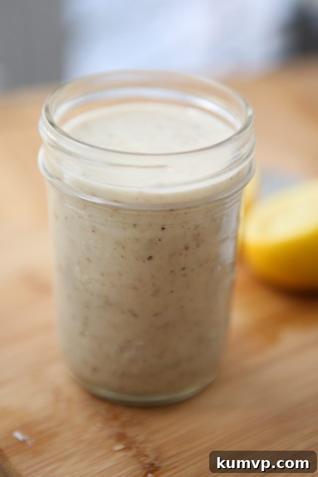 Mason jar full of Parmesan Walnut Lemon Vinaigrette on a wooden cutting board with a lemon half in the background