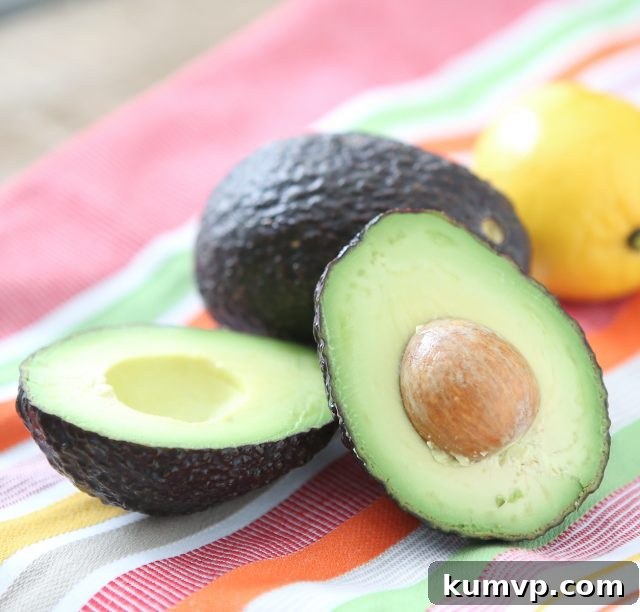 avocado sliced in half on a tablecloth next to a whole avocado and lemon