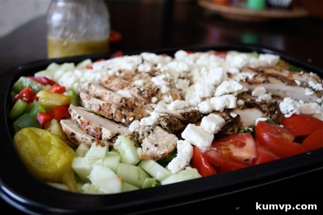Close-up of freshly grilled chicken alongside diced cucumbers, ripe tomatoes, vibrant pepperoncini, and crumbled feta cheese, ready for a delicious Greek salad.