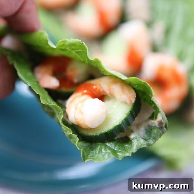 A close-up view of a single romaine lettuce leaf, tightly packed with juicy sriracha shrimp and crisp cucumber slices, with a tempting drizzle of hot sauce, highlighting the fresh and vibrant ingredients of this healthy meal