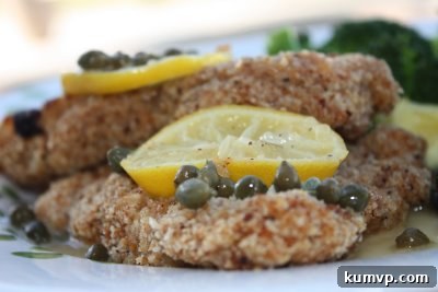 Ina Garten Chicken Piccata served on a plate with fresh garnishes A plated serving of chicken piccata, showing the golden chicken cutlet generously coated in lemon-caper sauce, with fresh lemon wedges and parsley