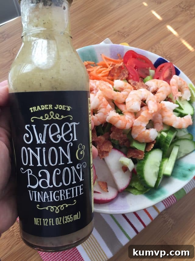 Garden Salad with Shrimp and Bacon A close-up view of a garden salad featuring crisp lettuce, colorful vegetables, shrimp, and bacon, with a hand gently holding a bottle of Trader Joe's Sweet Onion & Bacon Vinaigrette in the foreground, highlighting the suggested dressing for this delicious meal.