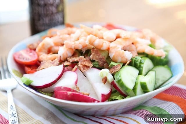 Garden Salad with Shrimp and Bacon A fresh and colorful bowl of garden salad, featuring a vibrant mix of green lettuce, halved cherry tomatoes, succulent shrimp, thinly sliced radishes, crisp cucumbers, and shredded carrots, presenting a perfectly balanced and appetizing meal.