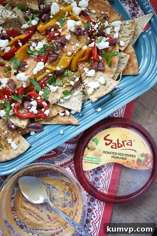 Close-up shot of homemade Mediterranean Nachos, showcasing the rich textures and colors of Sabra Hummus, crumbled feta, and fresh parsley on crispy pita chips.