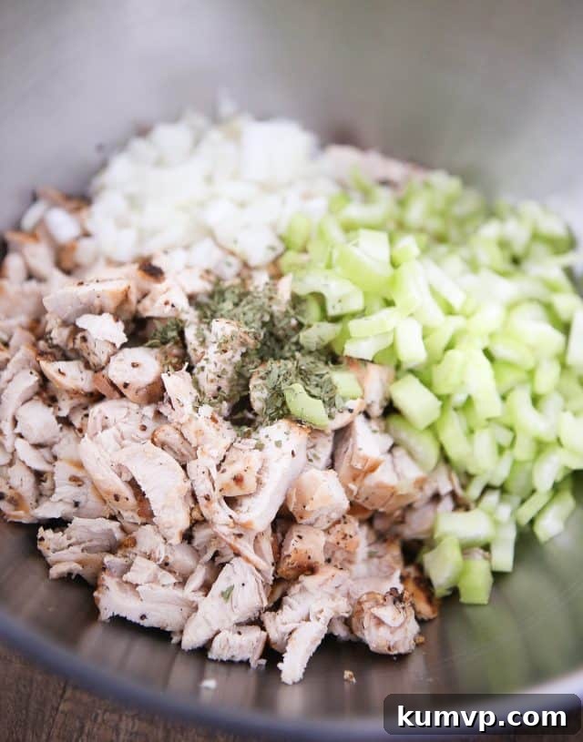 A large mixing bowl filled with diced grilled chicken, finely chopped sweet onions, crisp celery, and a medley of fresh seasonings, ready for the dressing.