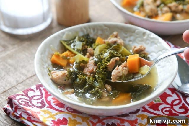 A close-up shot of a single bowl of Slow Cooker Italian Sausage and Kale Soup, showing the rich texture of the sausage, sweet potatoes, and vibrant kale, with a spoon resting in it.
