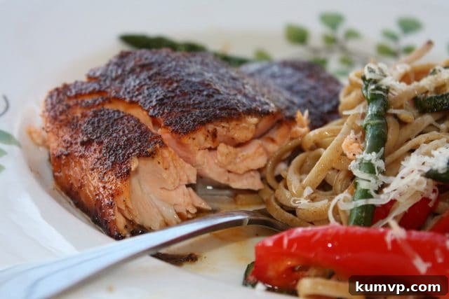 Healthy Salmon with Sweet Savory Rub: An Easy Broiled & Grilled Recipe for Your Family! Delicious piece of broiled salmon on a white plate, accompanied by a fork and a vibrant pasta dish with fresh vegetables.