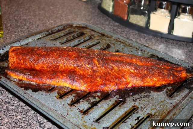 Prepare your salmon with this irresistible sweet and savory rub before broiling or grilling. Uncooked salmon fillet generously coated with a sweet and savory rub, resting on a roasting pan, ready for cooking.