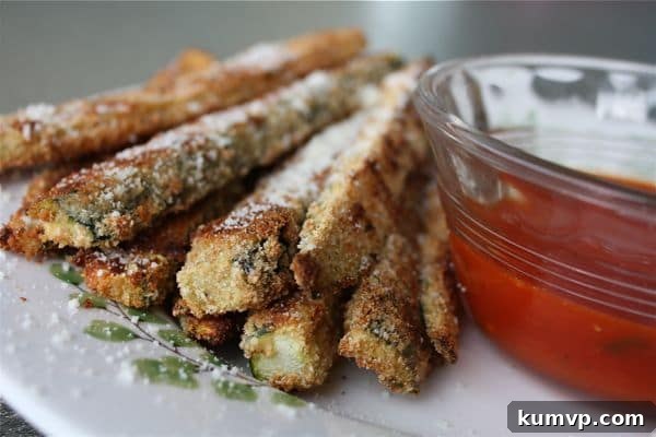 Serve these hot Oven Baked Parmesan Zucchini Sticks with your favorite dip! A serving of hot and crispy oven-baked Parmesan zucchini sticks with a bowl of marinara sauce.
