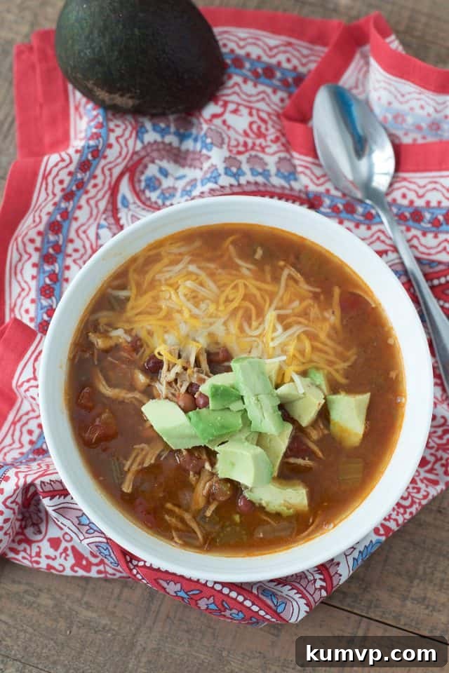 Instant Pot Mexican Chicken Soup Overhead shot of a bowl of Instant Pot Mexican Chicken Soup, generously topped with melted shredded cheese and fresh diced avocado, with a spoon ready for enjoyment on a red and blue napkin.