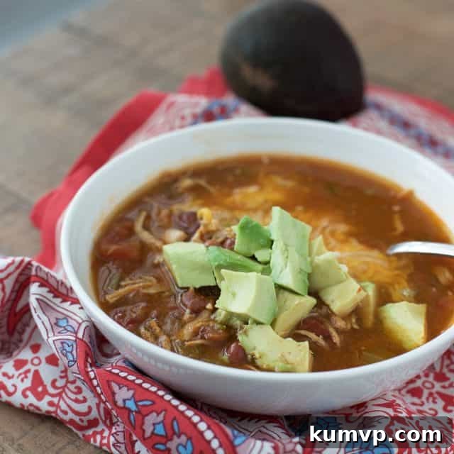 Instant Pot Mexican Chicken Soup A close-up shot of a white bowl filled with chili-flavored Instant Pot Mexican Chicken Soup, elegantly topped with freshly diced avocado, ready to be enjoyed as a wholesome and comforting meal.