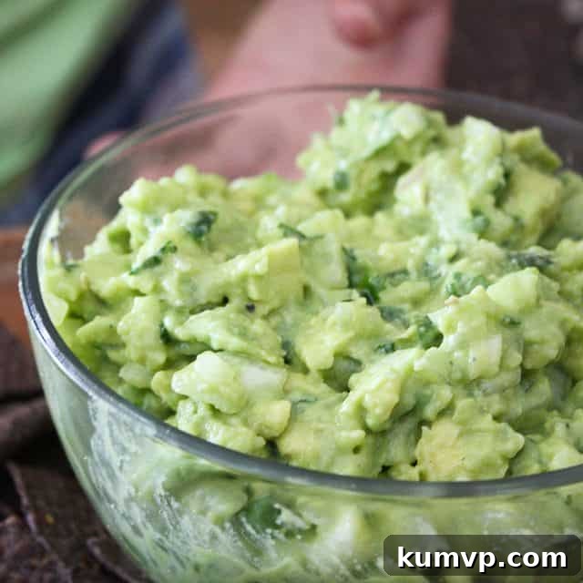 A bowl of the BEST Guacamole, rich, creamy, and vibrant green, topped with fresh cilantro, diced tomatoes, and a squeeze of lime. Perfect for dipping tortilla chips or fresh vegetables on Super Bowl Sunday.