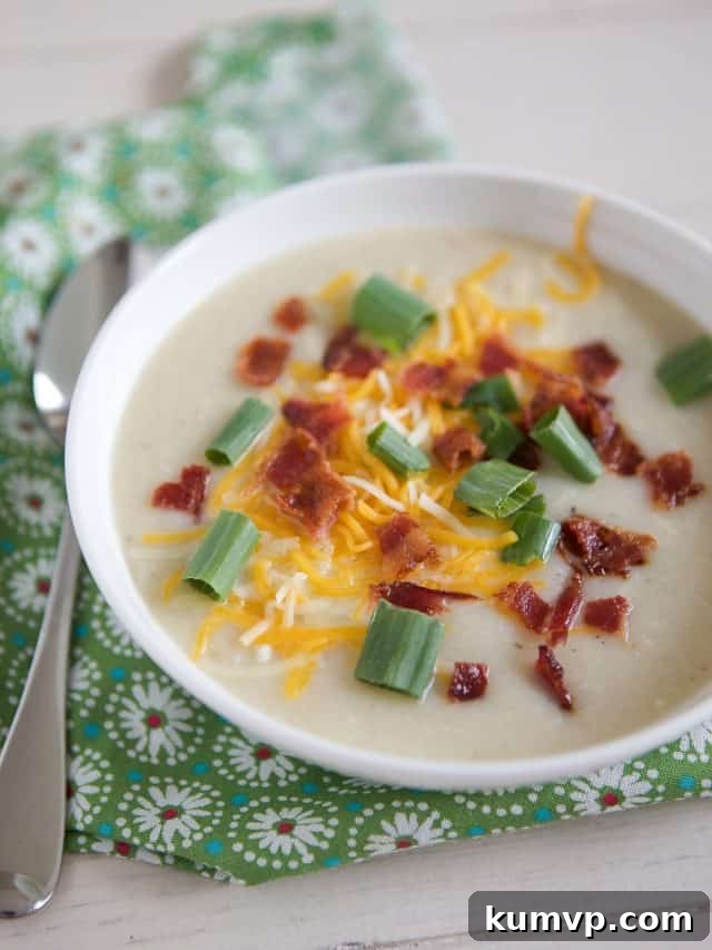 white bowl filled with cauliflower potato soup topped with cheese, green onion and bacon