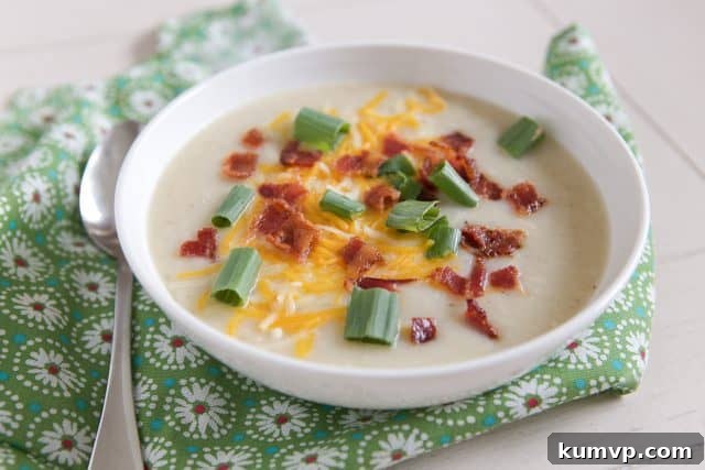 white bowl filled with cauliflower potato soup topped with cheese, green onion and bacon