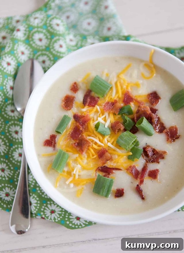 overhead shot of white bowl filled with cauliflower potato soup topped with cheese, green onion and bacon