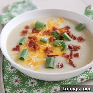 White bowl filled with cauliflower potato soup topped with cheese, green onion and bacon