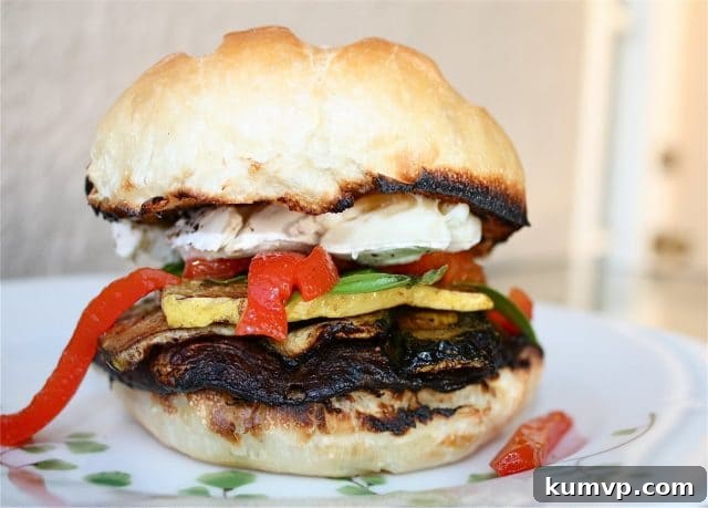 A hand holding a beautifully crafted Grilled Portabella and Brie Burger, poised for a delicious bite, showcasing its impressive height and fresh ingredients.