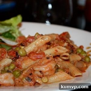 A close-up shot of creamy shrimp pasta with tomatoes and peas in a white bowl, garnished with fresh parsley.