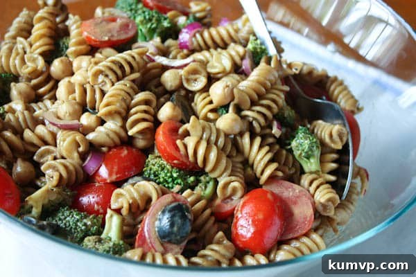 Vibrant pasta salad with cherry tomatoes, olives, red onions, and fresh broccoli, drizzled with balsamic basil vinaigrette