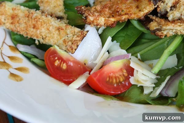 Spinach and Eggplant Salad plate of spinach salad topped with cherry tomatoes, red onion, shredded cheese, and baked breaded eggplant