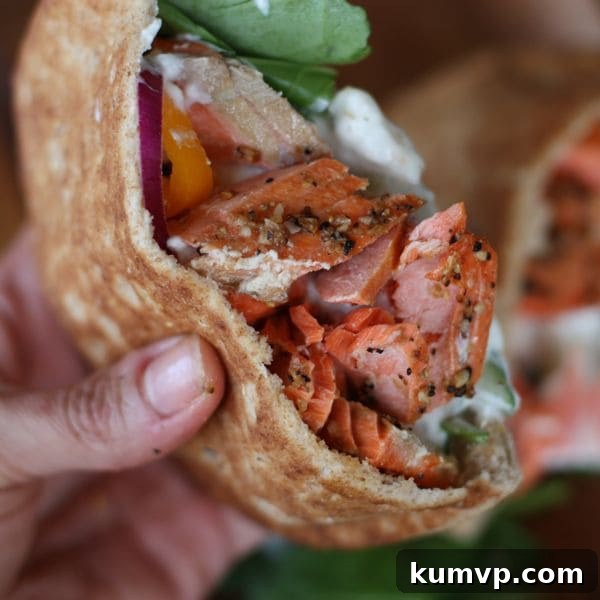 pita cut in half stuffed with broiled salmon and a white sauce with a side of spinach