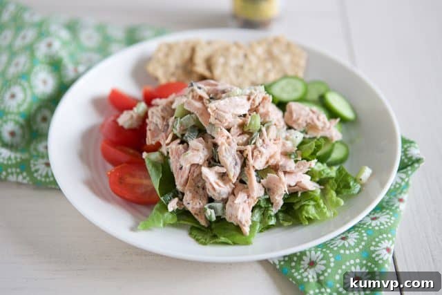 Easy Salmon Salad Recipe white plate filled with tomatoes, cucumbers and lettuce topped with salmon salad