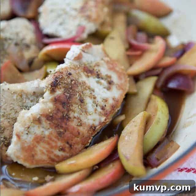 Close-up of golden brown pork chops with caramelized apples and onions in a cast iron skillet, ready to serve.
