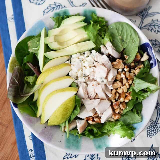 overhead photo of salad plate with greens, sliced pear, sliced avocado, chopped rotisserie chicken and walnuts