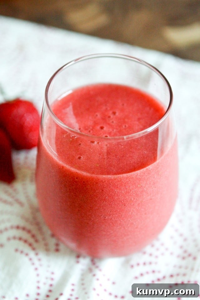 Strawberry, Grapefruit & Ginger Smoothie for Energy A vibrant Strawberry, Grapefruit, and Ginger Smoothie in a tall glass, garnished with a fresh strawberry and a slice of grapefruit, sitting on a light wooden surface. It promises a refreshing energy boost any time of day.