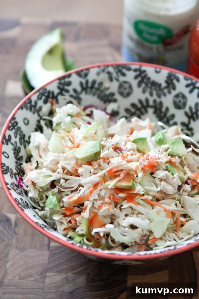 bowl of chicken slaw salad topped with buffalo sauce with a container of blue cheese and half of an avocado in the background